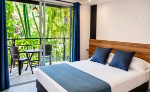 Ein Hotelzimmer mit Bett, einem Balkon mit Tisch und Stühlen und Blick auf Grünflächen.