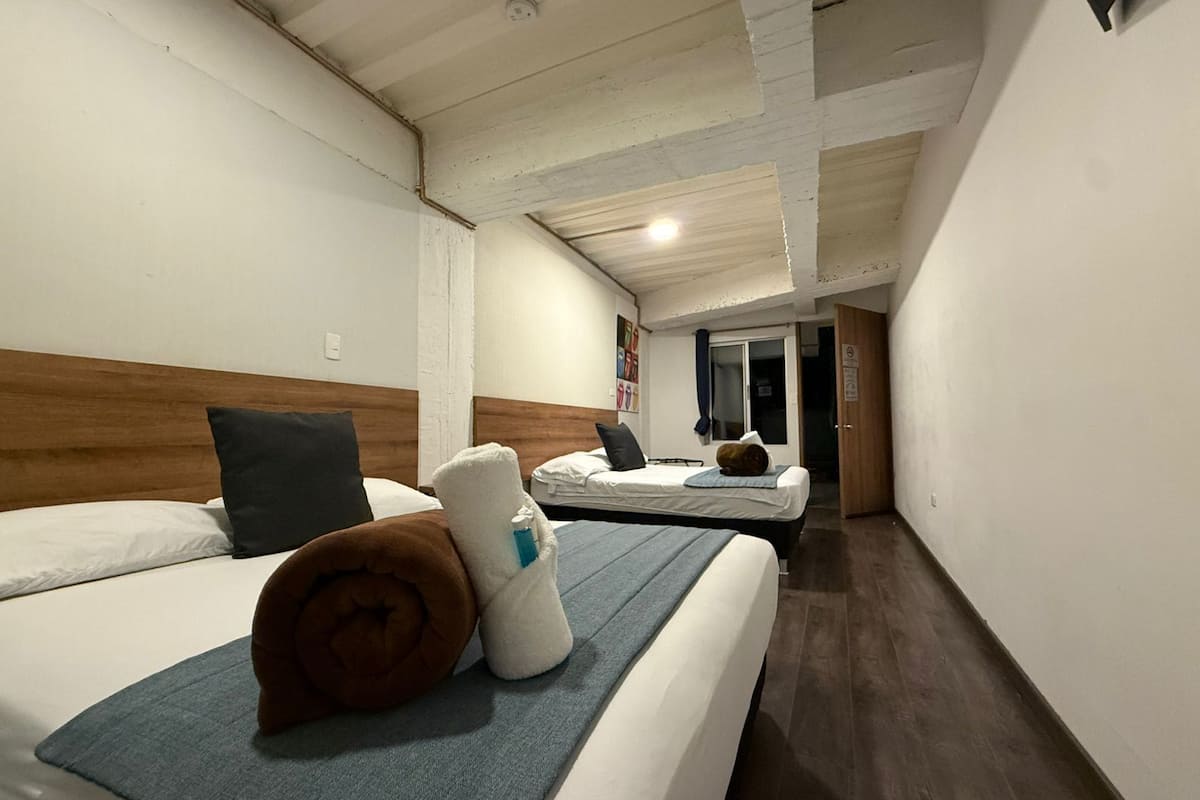 Habitación de hotel con dos camas, cabecero de madera, manta azul y una toalla sobre la cama.