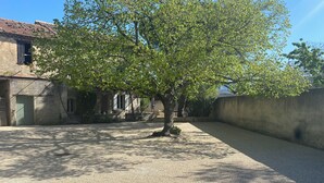 A courtyard with a tree, a building with a tiled roof, and a concrete wall. - Provencal house with heated pool between Luberon & Alpilles - absolute calm (Cheval-Blanc)