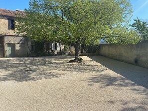 A courtyard with a tree, a building with a tiled roof, and a concrete wall. - Provencal house with heated pool between Luberon & Alpilles - absolute calm (Cheval-Blanc)