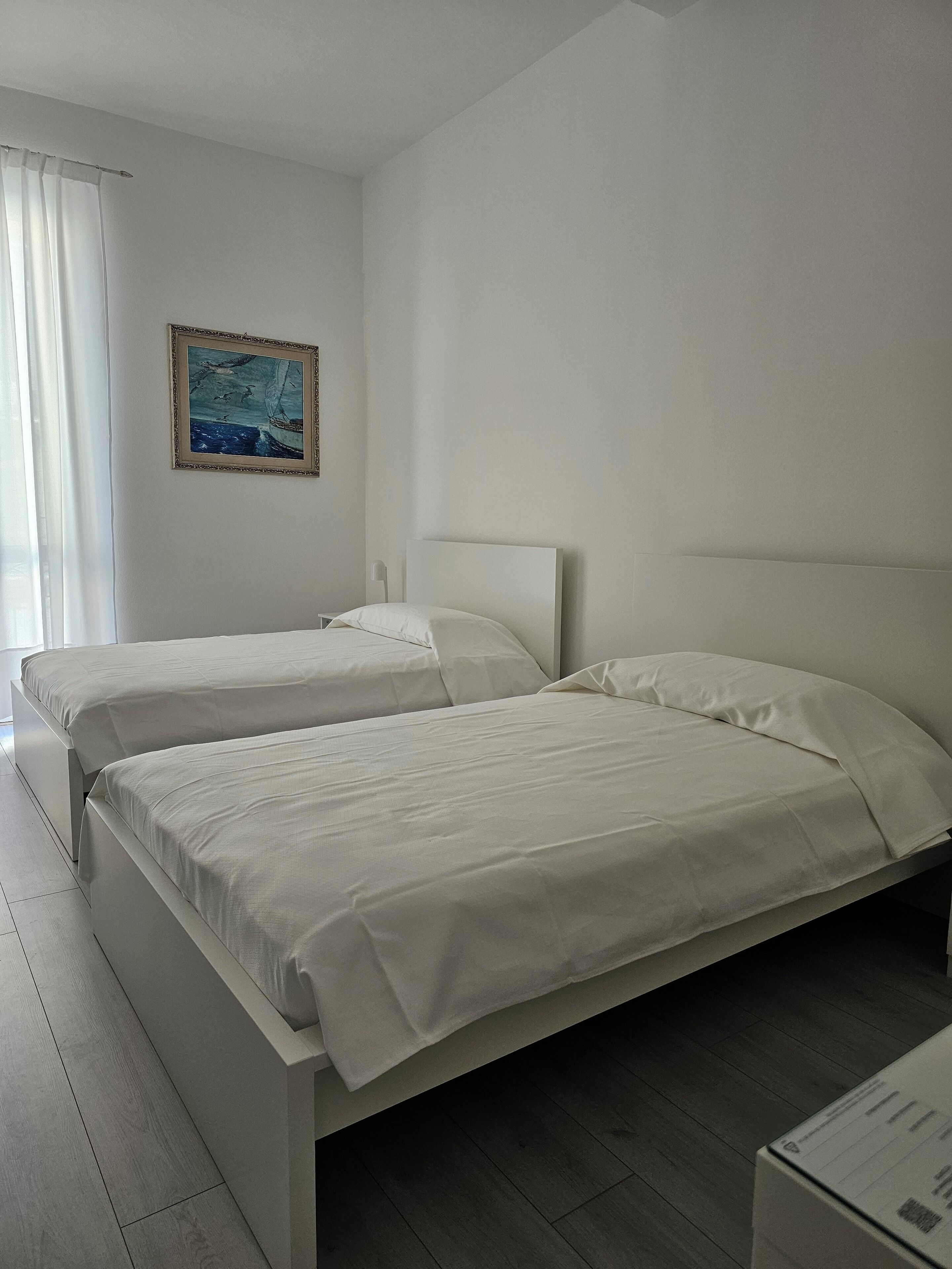 A hotel room with two beds, a painting on the wall, and a window with curtains.
