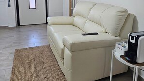 Un salon avec un canapé beige, un tapis tissé, une machine à café et un tableau encadr é accroché au mur.