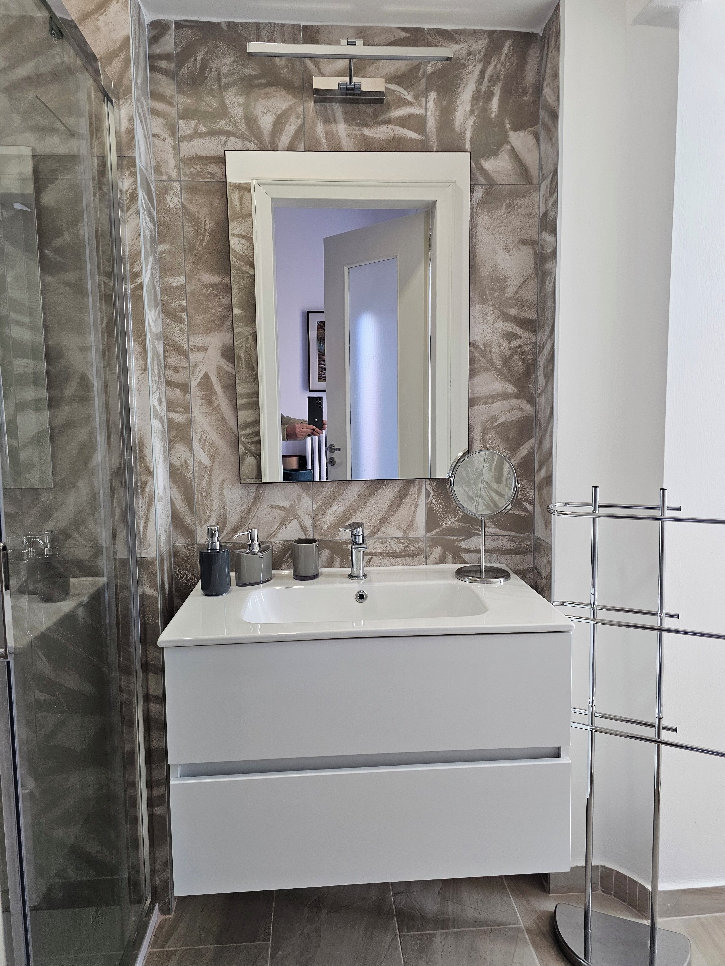 Ein modernes Badezimmer mit einem großen Spiegel, einem weißen Waschbecken und einer Duschkabine aus Glas.