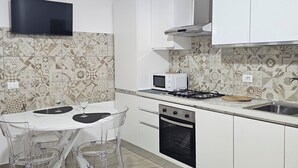Une cuisine moderne avec des meubles blancs, un téléviseur à écran plat, un four à micro-ondes, une cuisinière à gaz et un évier.