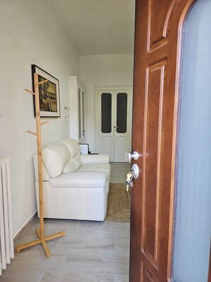 A modern living room with a white sofa, a wooden floor lamp, and a framed picture on the wall. - Brand new semi-central apartment very convenient to services (Novara)
