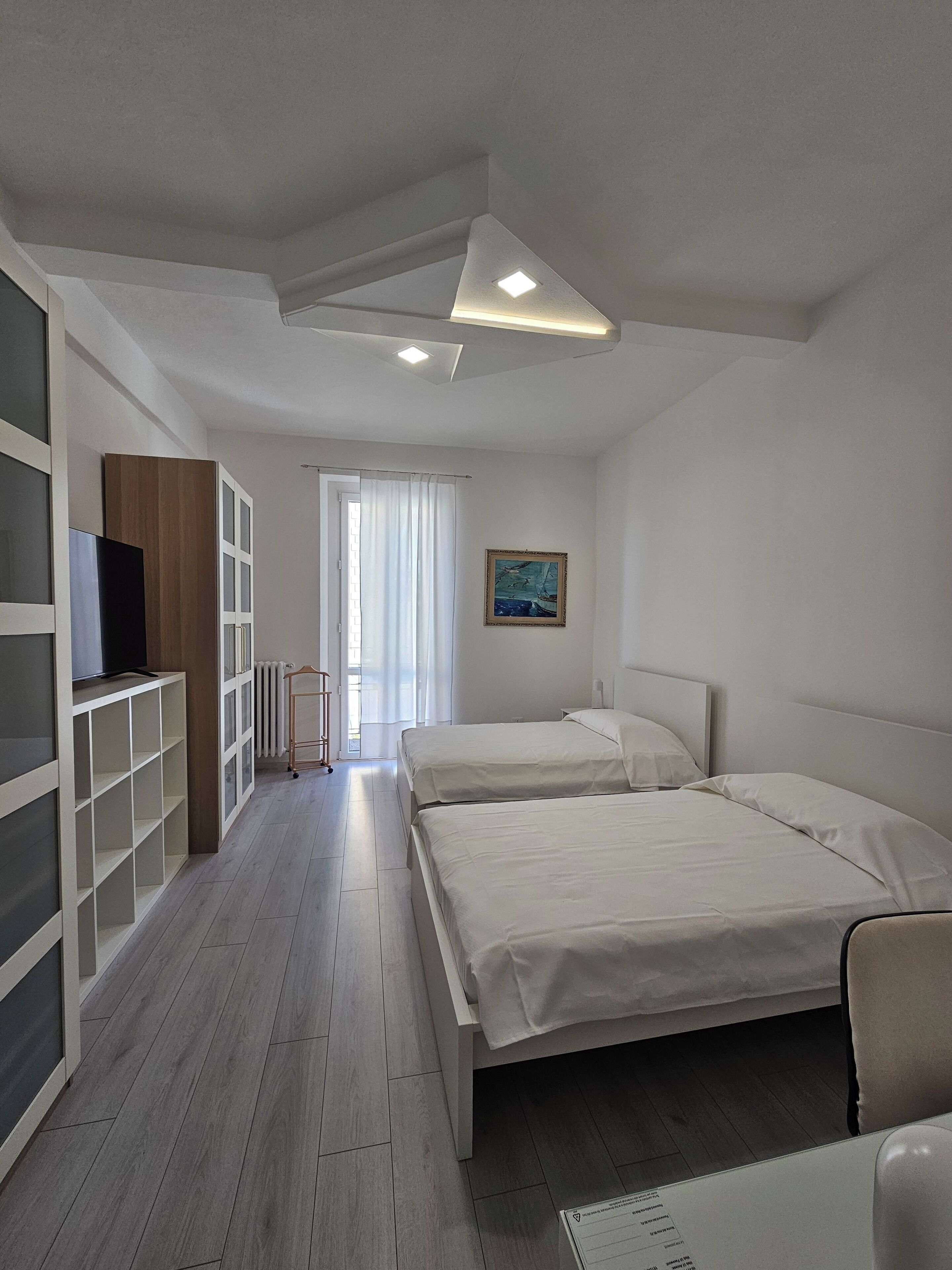 Una habitación de hotel moderna con dos camas, un televisor en estante empotrado, un radiador y un cuadro en la pared.