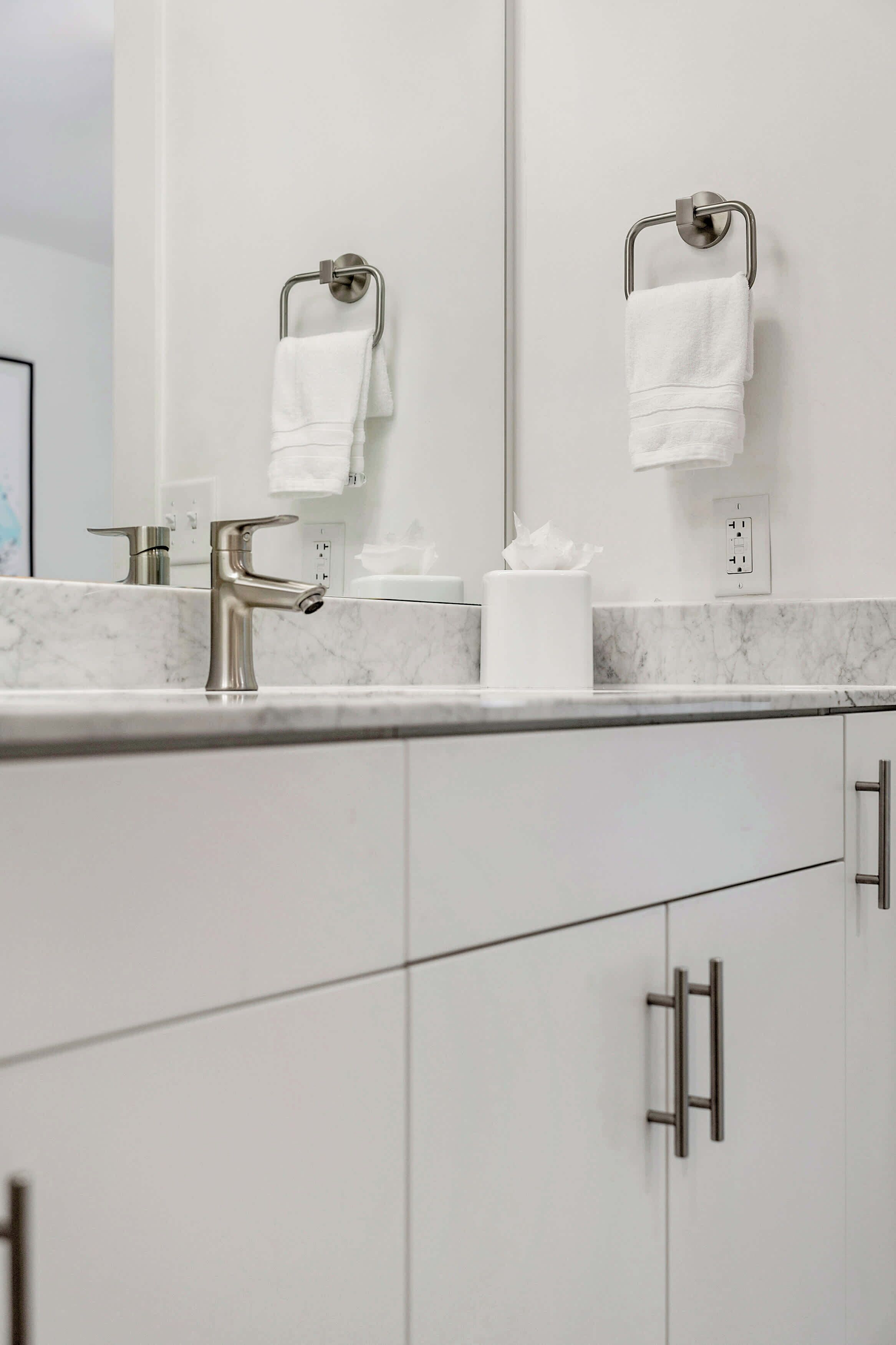 Une salle de bain moderne avec un comptoir en marbre, un lavabo avec un robinet chromé et un miroir au-dessus. On y trouve deux porte-serviettes avec des serviettes blanches et un rouleau de papier toilette sur le comptoir.
