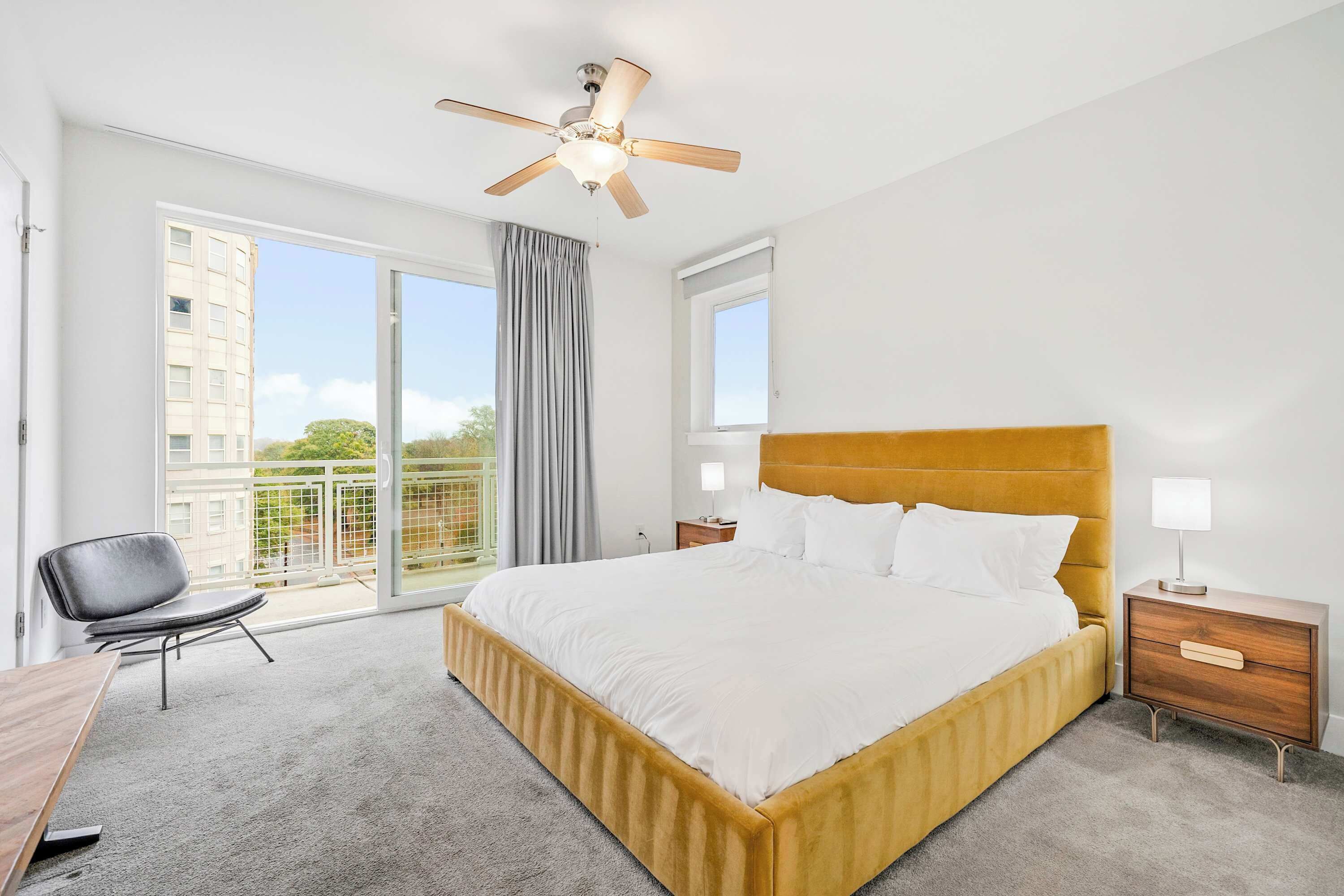 A hotel room with a large bed, a desk, a chair, a nightstand, a lamp, and a ceiling fan.