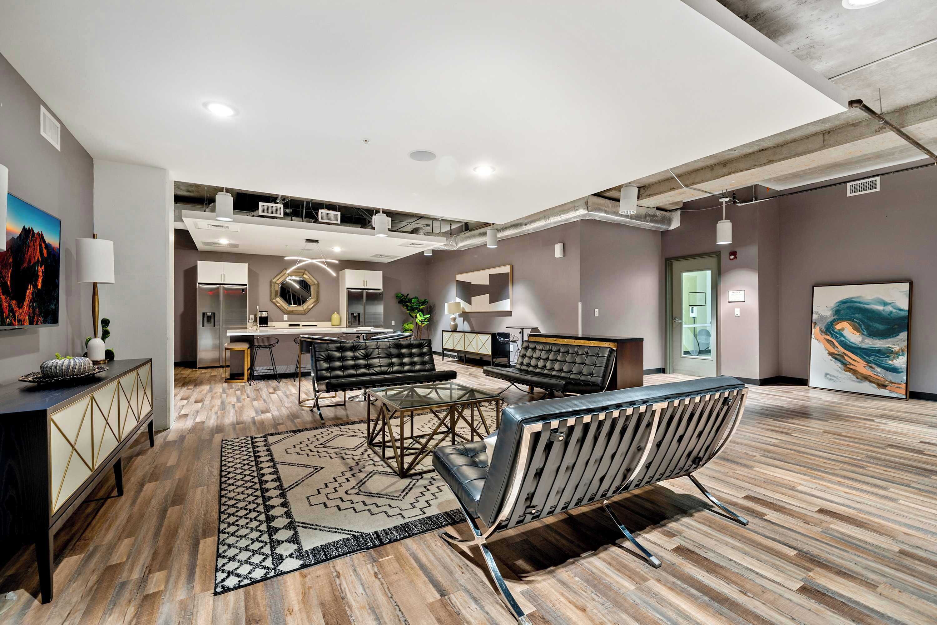 A spacious living area with a modern kitchen in the background, a dining area with a glass table, and a large abstract painting on the wall.