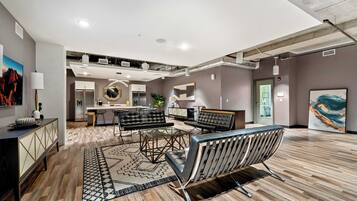 A spacious living area with a modern kitchen in the background, a dining area with a glass table, and a large abstract painting on the wall.