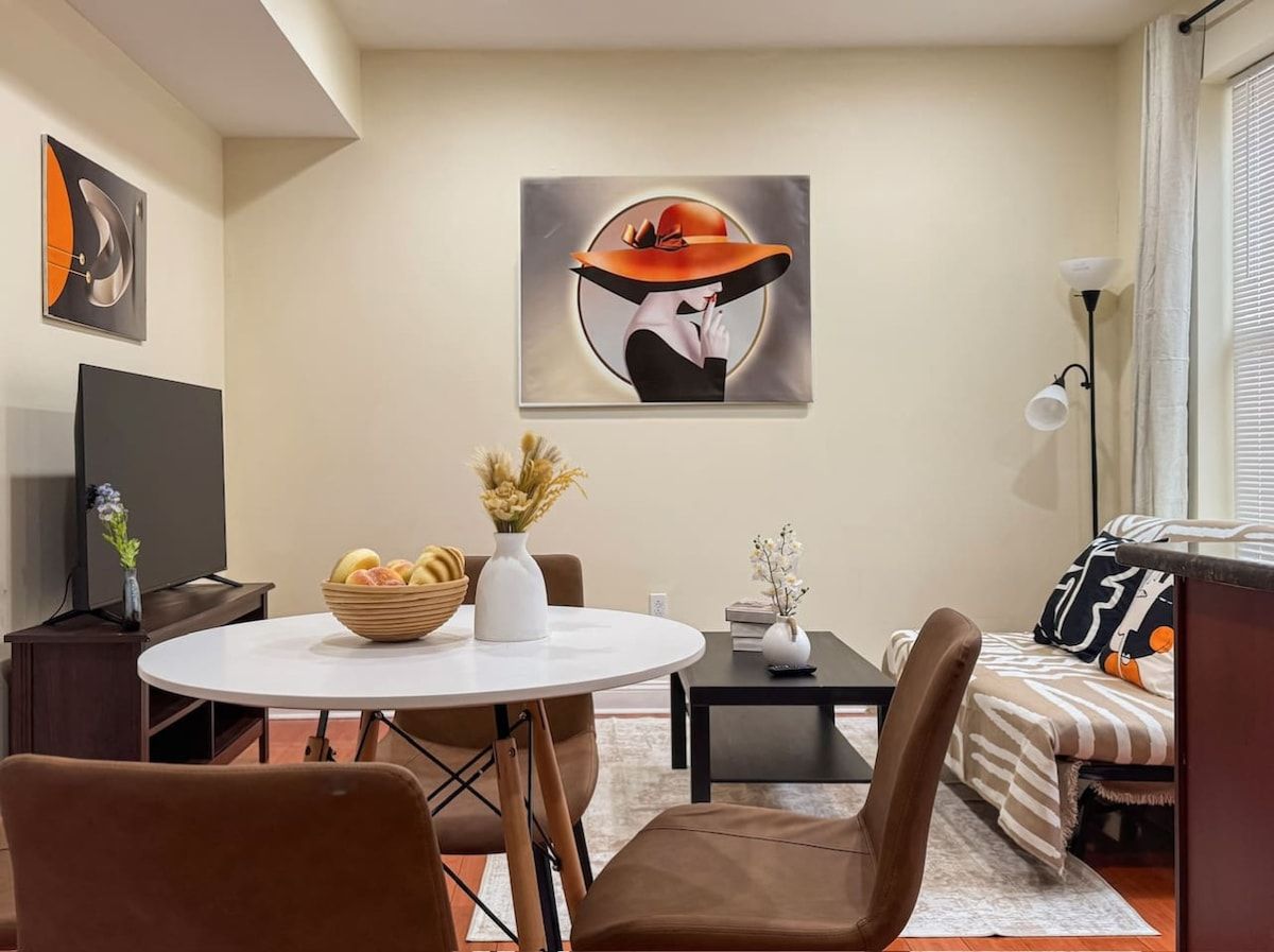 A modern living room with a round dining table, brown chairs, a sofa, and a flat-screen TV.