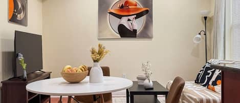 A modern living room with a round dining table, brown chairs, a sofa, and a flat-screen TV.