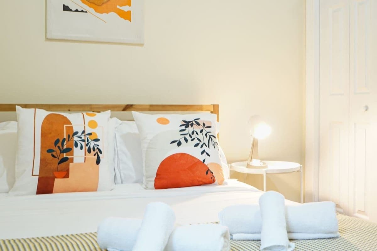 Una cama bien hecha con almohadas, una lámpara de noche y toallas enrolladas, con un edredón a rayas.