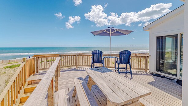 Een houten terras met twee stoelen en een tafel, met uitzicht op het strand.