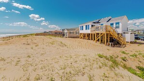 Een strandhuis met een houten terras en een trap naar een tweede verdieping.