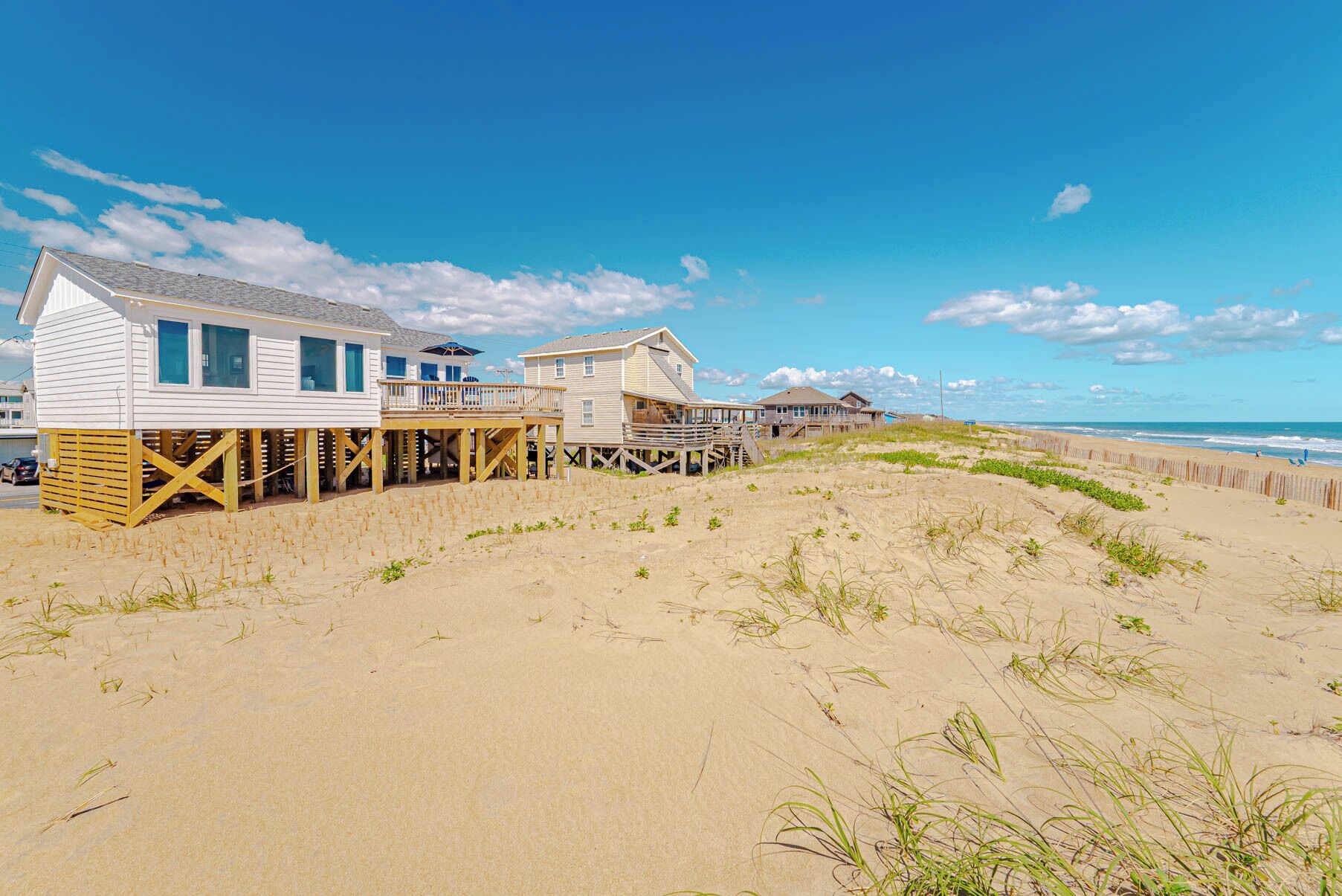 Une propriété située en bord de mer, dotée d’une terrasse en bois, d’une maison et d’une plage en arrière-plan.