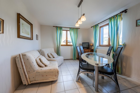 Une pièce comprenant un canapé, une table à manger avec des chaises, un téléviseur et des rideaux.