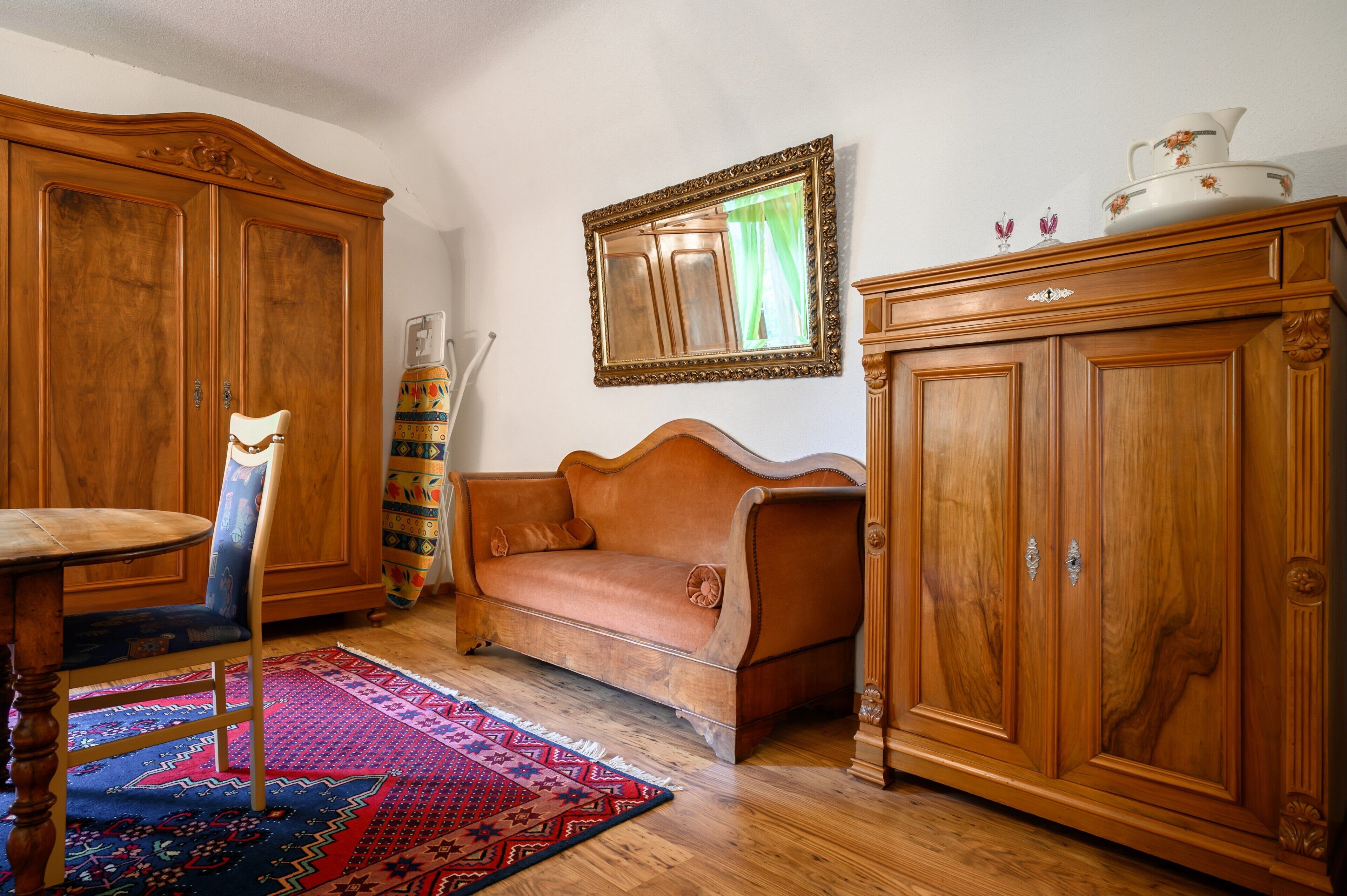 Um quarto com um armário de madeira, um sofá, uma cadeira e um tapete estampado.