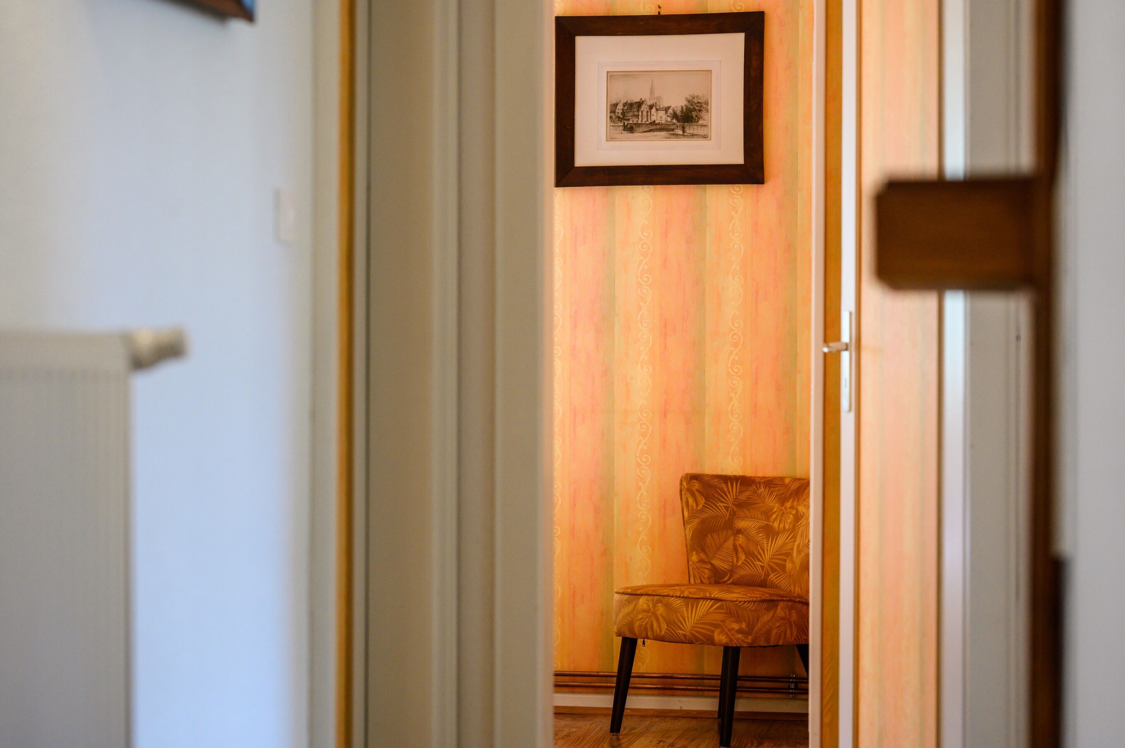 Un corridoio con una sedia, un quadro incorniciato appeso al muro e una porta.