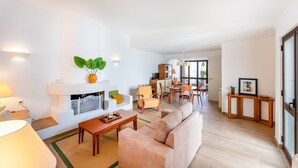 Sala de estar con chimenea, sofá, mesa de centro y zona de comedor con sillas y una mesa.
