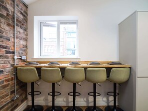 A kitchen with a brick wall, a window, a wooden countertop, and four bar stools. - Serge | The Heim (Greater Manchester)
