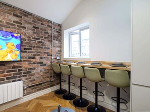 A kitchen with a brick wall, a window, and bar stools. - Serge | The Heim (Greater Manchester)