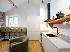 A modern kitchen with a large window, a built-in oven, and a bar area with stools. - Serge | The Heim (Greater Manchester)