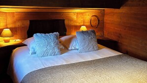 Ein gemütliches Schlafzimmer in einer Holzhütte mit einem großen Bett, zwei Nachttischen und einer runden Wandlampe.