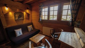 Ein gemütliches Blockhaus-Interieur mit einer Holzcouch, einem Esstisch und einem Sessel.
