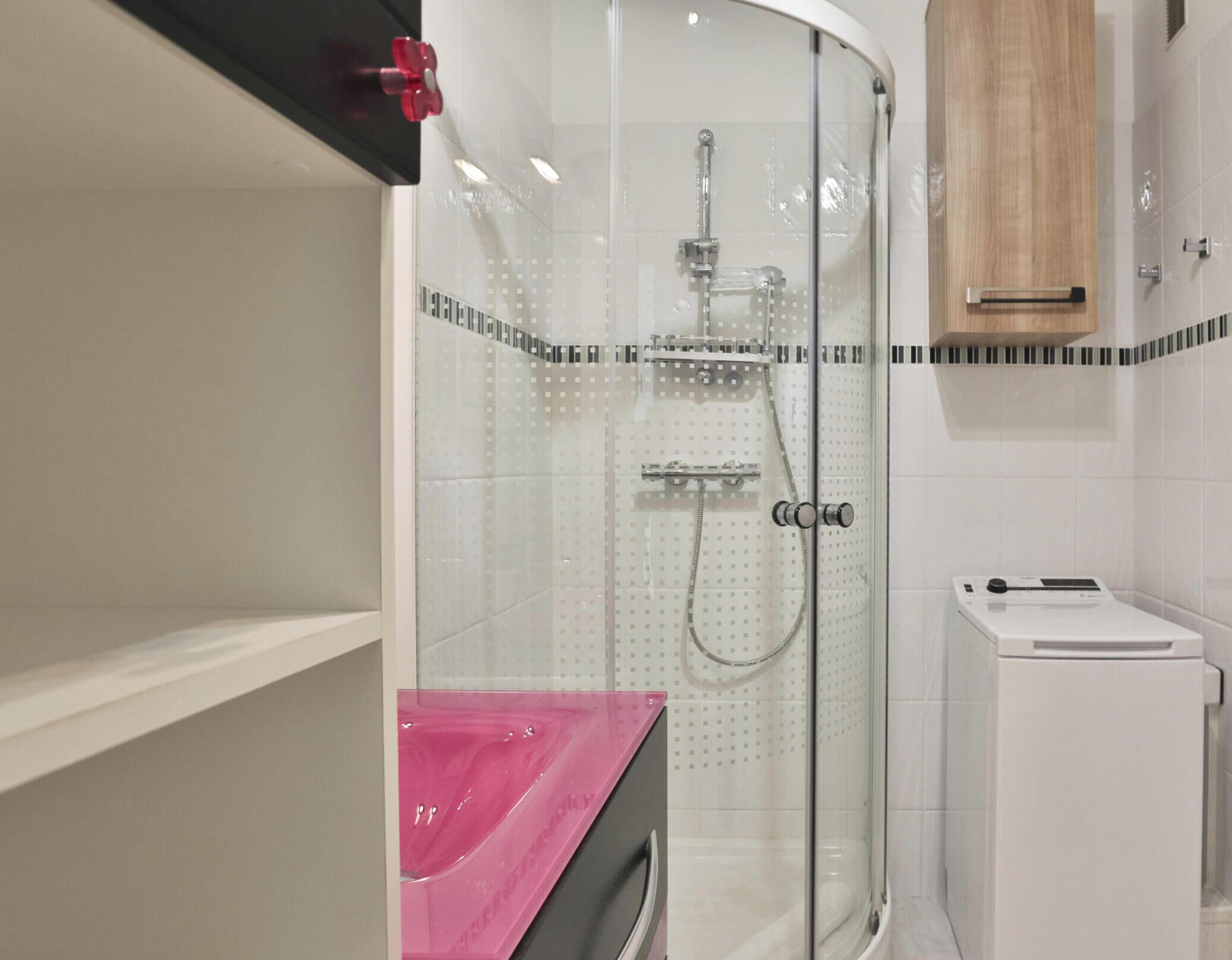 A bathroom with a glass-enclosed shower, a white washing machine, and a wooden cabinet.