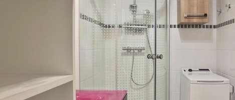 A bathroom with a glass-enclosed shower, a white washing machine, and a wooden cabinet.