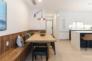 A modern kitchen with a wooden bench, a dining table, and a pendant light. - Max Send (Revelstoke)