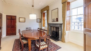 A dining room with a wooden table, chairs, a chandelier, a fireplace, and large windows with curtains. - Spacious, central, top floor, period apartment w/park views (Edinburgh)