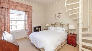 A bedroom with a bed, bedside table, lamp, and a white ladder. - Spacious, central, top floor, period apartment w/park views (Edinburgh)