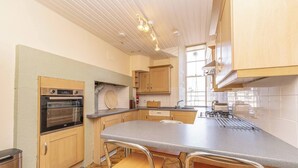 A kitchen with a built-in oven, a large island with stools, and wooden cabinets. - Spacious, central, top floor, period apartment w/park views (Edinburgh)
