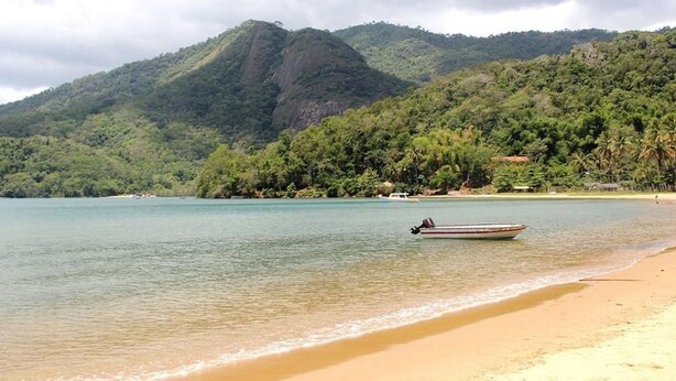 A beach with a boat on the water and mountains in the background. - Casa com Ar e Wi-fi pr Xima Praia da Tapera (Florianópolis)