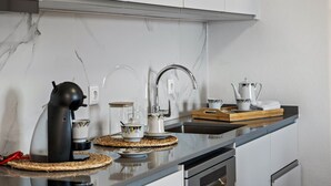 A modern kitchen with a sleek black countertop, white cabinets, a stainless steel sink, and a coffee machine. - John's Villa by Homie (Canhas)