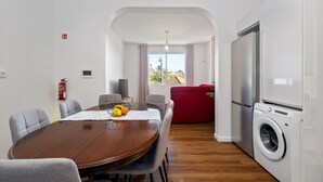 A modern living room with a wooden dining table, grey chairs, a red sofa, a washing machine, and a large TV. - John's Villa by Homie (Canhas)