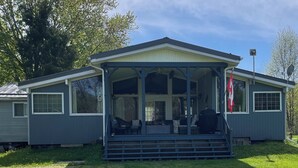 A single-story house with a covered porch, a flag, and a satellite dish. - Peaceful riverside cottage-Tranquil views & private outdoor space (Tweed)