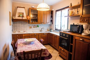 Una cucina con mobili in legno, zoccolo a mosaico, un tavolo da pranzo con tovaglia e un forno a microonde.