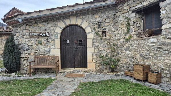 Un edificio de piedra con una puerta de madera grande, un banco y cajas de madera en el exterior.