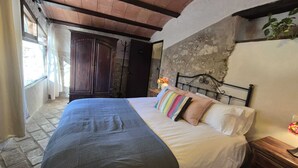 Une chambre à coucher avec un lit, une armoire en bois, un mur en pierre et une fenêtre.