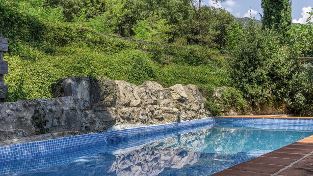 Une piscine aux carreaux bleus, entourée d’un mur de pierre et d’une végétation luxuriante.