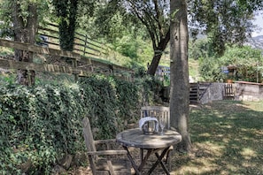 A rustic outdoor seating area with a wooden table and chairs, surrounded by lush greenery and a wooden fence. - Real disconnection in Alta Garrotxa. Nature, calm and home cooking. (Oix)
