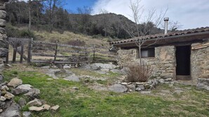 Un bâtiment rustique en pierre, avec un toit en tuiles, une clôture en bois et un paysage rocheux.