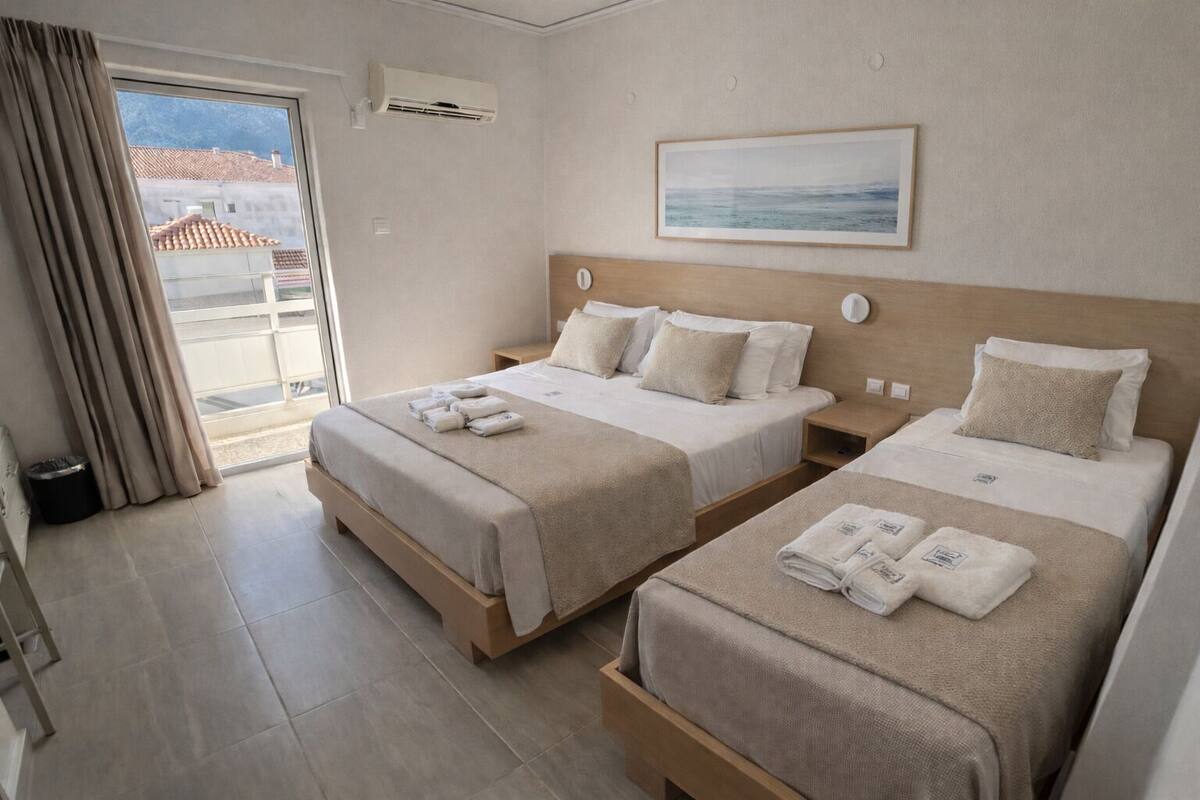 A hotel room with two beds, a window with curtains, a framed picture on the wall, and an air conditioning unit.