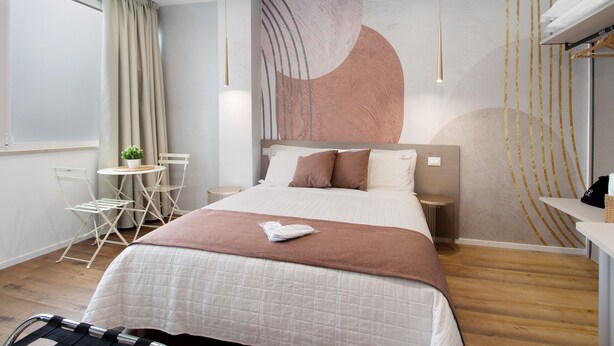 A modern hotel room with a large bed, a small round table with chairs, a bedside table, and a wall with abstract art. - Room 3 - Anita Rooms Bari (Bari)