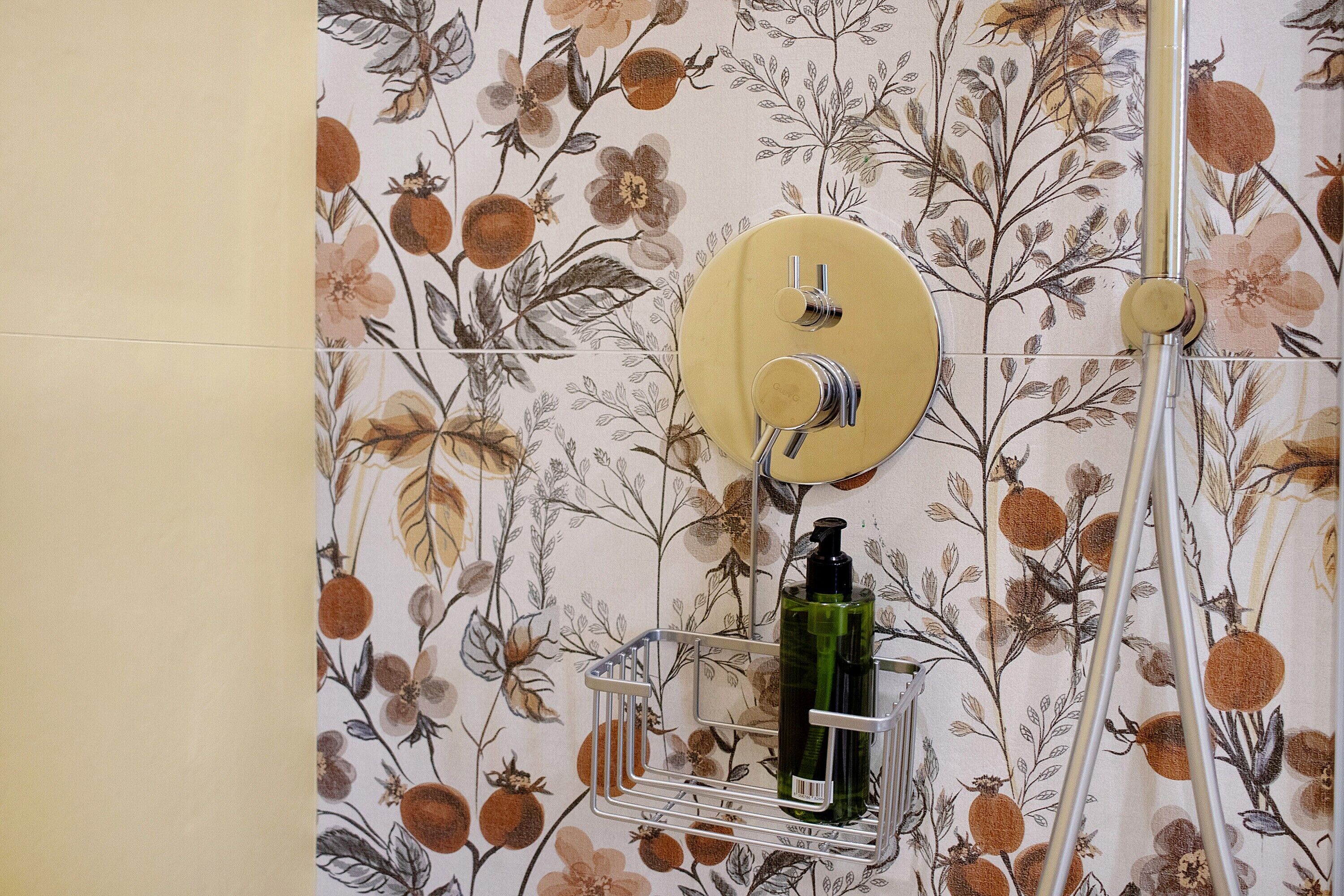 Ein Badezimmer mit floralem Wandpapier, einer Duschbrause und einer Flasche in einem Metallgestell.