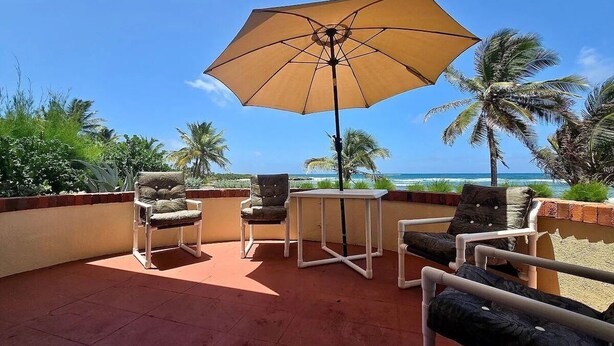 A terrace with a table, chairs, and an umbrella overlooking a beach. - Oceanfront retreat in with AC and pool (Inch Marlow)