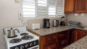 A compact kitchen with a stove, toaster, coffee maker, kettle, and a small sink. - Oceanfront retreat in with AC and pool (Inch Marlow)